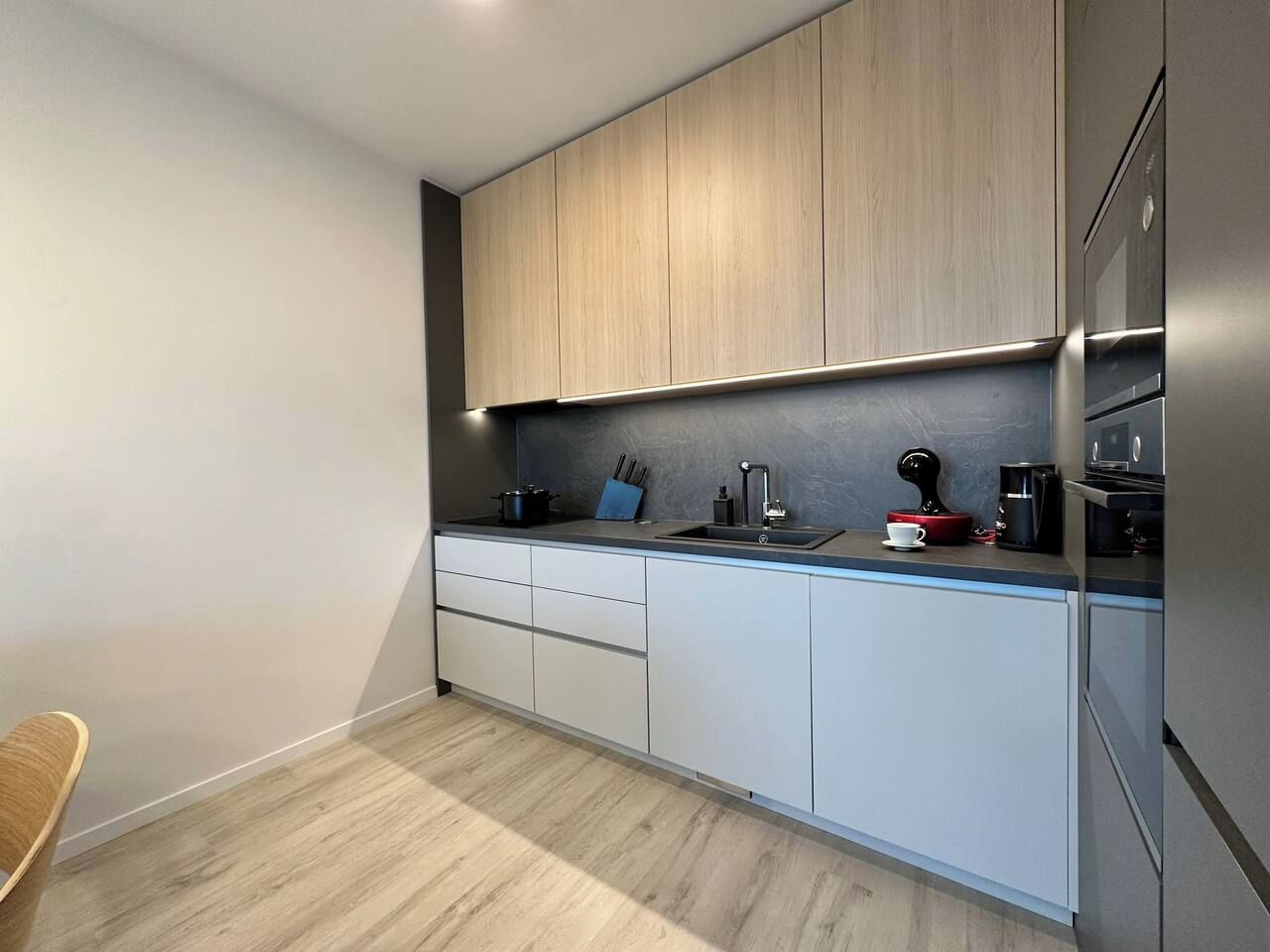 Una cocina moderna con armarios de madera clara, encimera oscura y electrodomésticos de acero inoxidable.