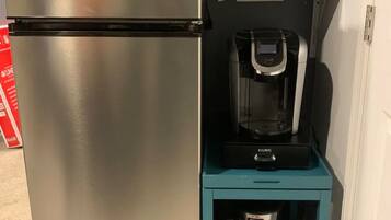 Een compact keukenhoekje met een roestvrijstalen koelkast, een koffiezetapparaat en een magnetron op een blauwgroen plank.