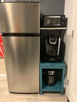 Une petite cuisine équipée avec un réfrigérateur en acier inoxydable, une machine à café et un four à micro-ondes, le tout placé sur une étagère de couleur turquoise.