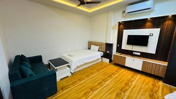 A modern hotel room with a bed, a sofa, a TV, and an air conditioning unit.