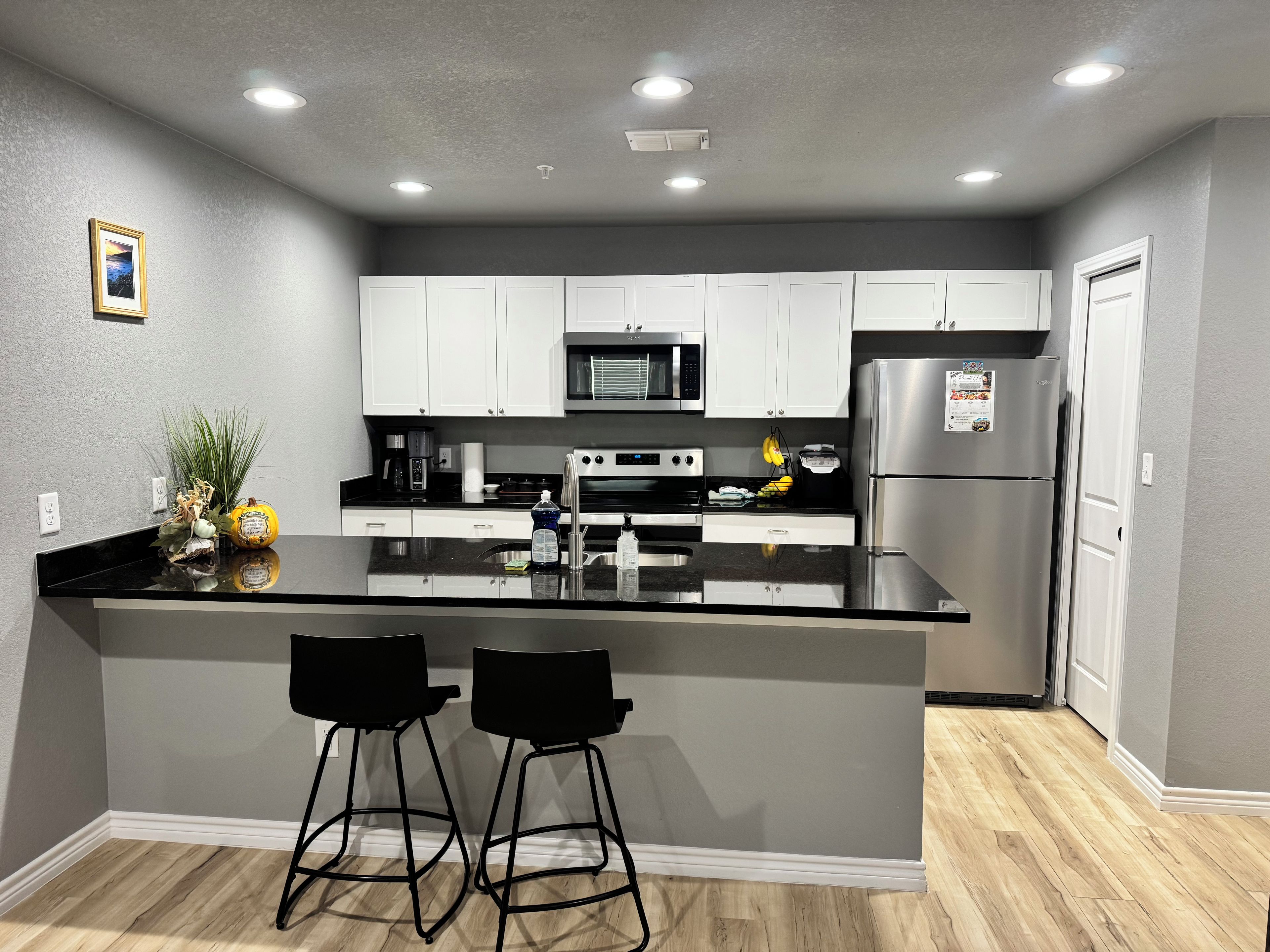 A modern kitchen with a central island, stainless steel appliances, and black bar stools.