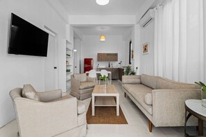 Un soggiorno moderno con una televisione a schermo piatto, due divani, un tavolino da caffè e una cucina sullo sfondo.
