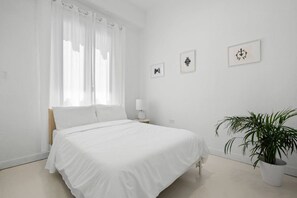 Una camera da letto minimalista con un letto, un comodino, una lampada e una pianta in vaso.