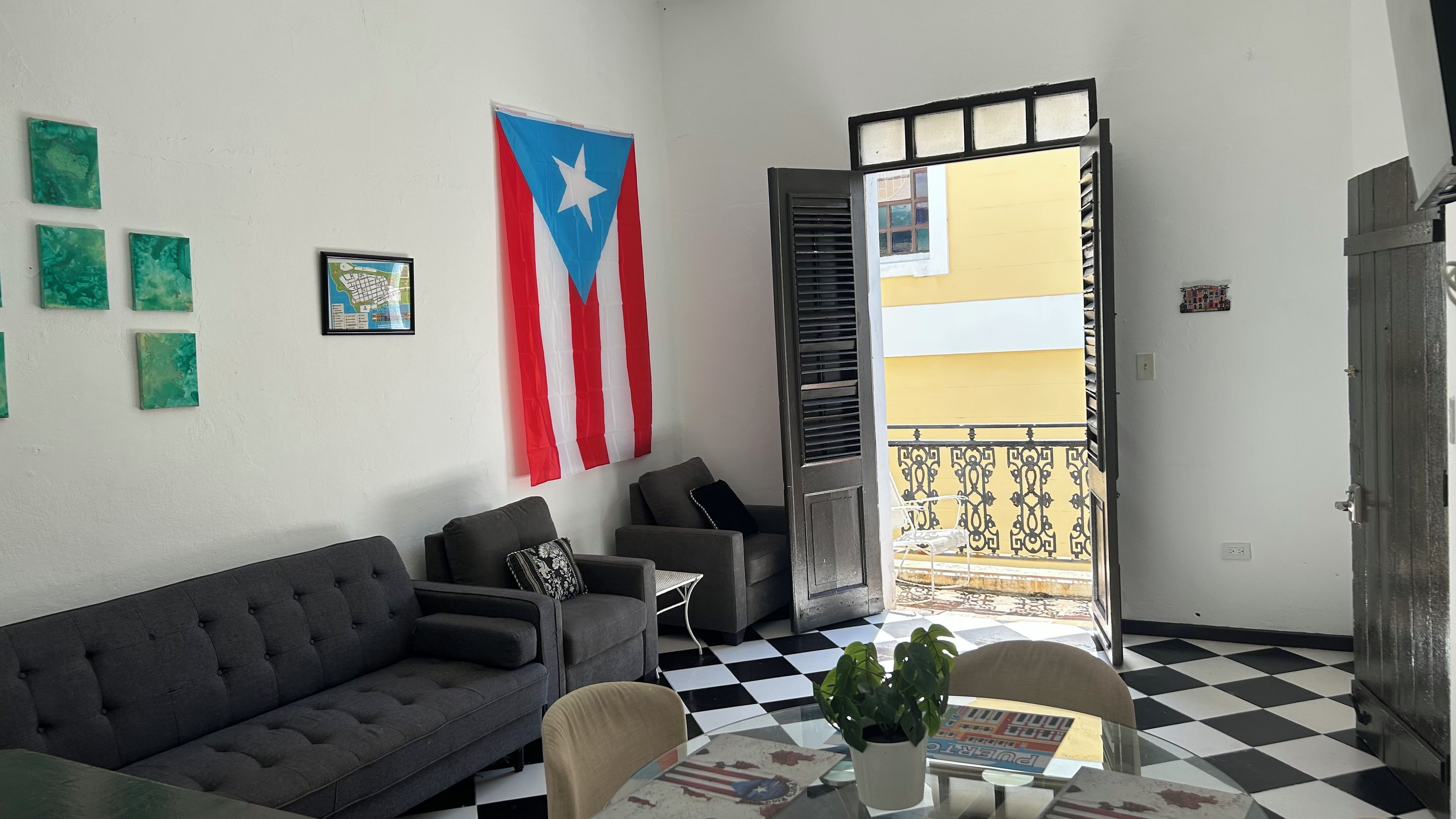 A living room with a sofa, a coffee table with a plant, a flag on the wall, and a balcony with a railing.