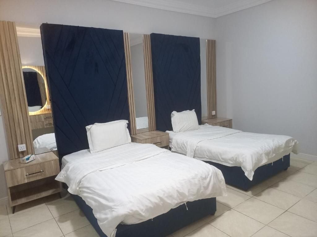 A hotel room with two single beds, a nightstand with a lamp, and a mirror above the bed.