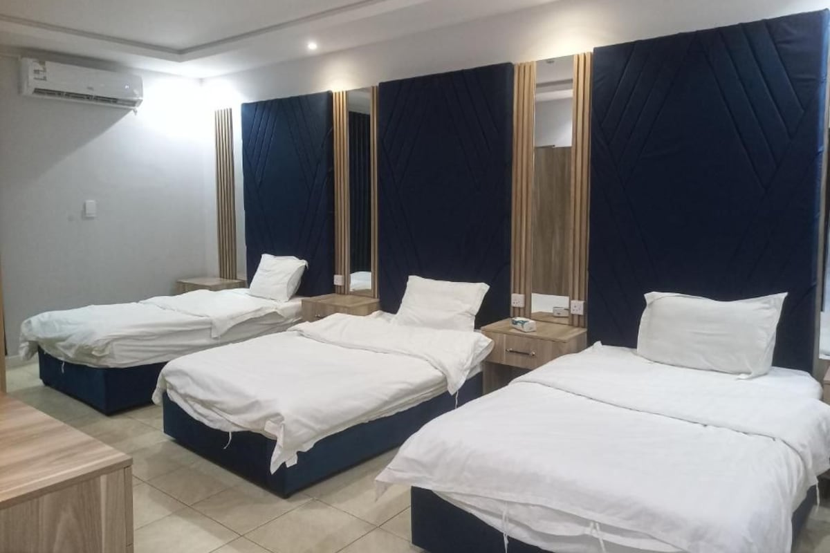 A hotel room with four single beds, a wooden nightstand, a mirror, and an air conditioning unit.