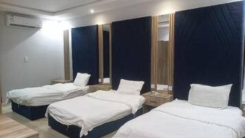 A hotel room with four single beds, a wooden nightstand, a mirror, and an air conditioning unit.