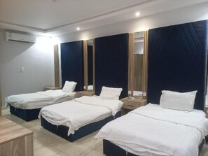 A hotel room with four single beds, a wooden nightstand, a mirror, and an air conditioning unit. - Fouad Ali Al-Ezzi for Serviced Apartments Al-Hawiyah (At Taif)