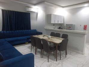 A modern living room with a blue sofa, a dining table with chairs, and a kitchen area with cabinets. - Fouad Ali Al-Ezzi for Serviced Apartments Al-Hawiyah (At Taif)