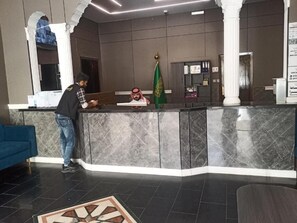 A reception area with a marble counter, a flag, and a blue sofa. - Fouad Ali Al-Ezzi for Serviced Apartments Al-Hawiyah (At Taif)