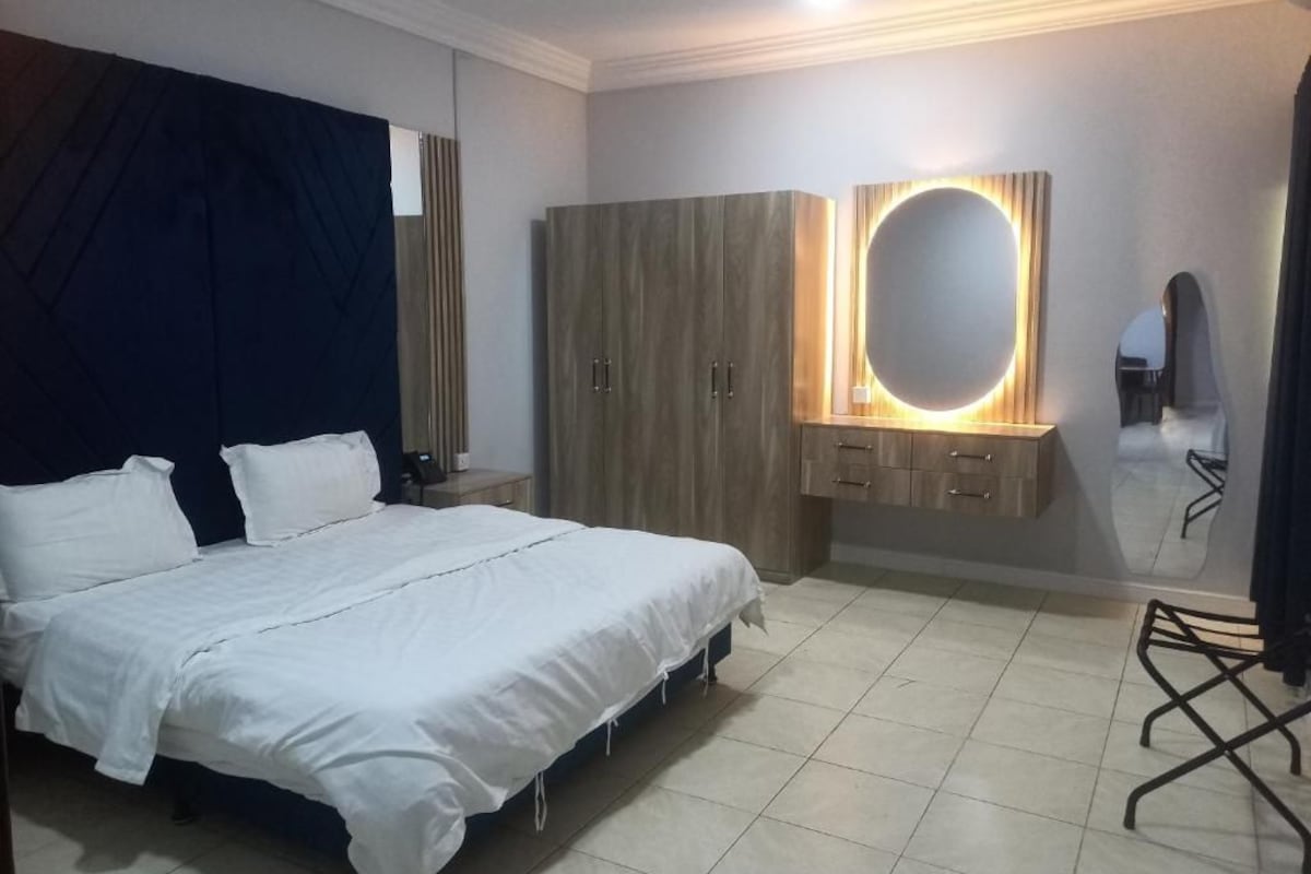 A bedroom with a bed, wardrobe, vanity with mirror, and a chair.