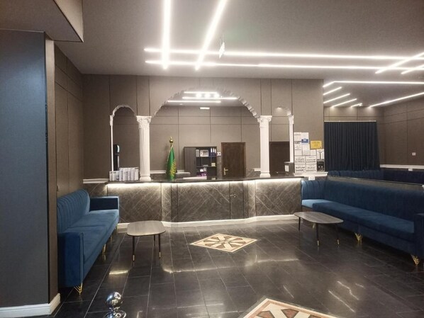 A modern lobby with a reception desk, blue sofas, and a patterned floor.