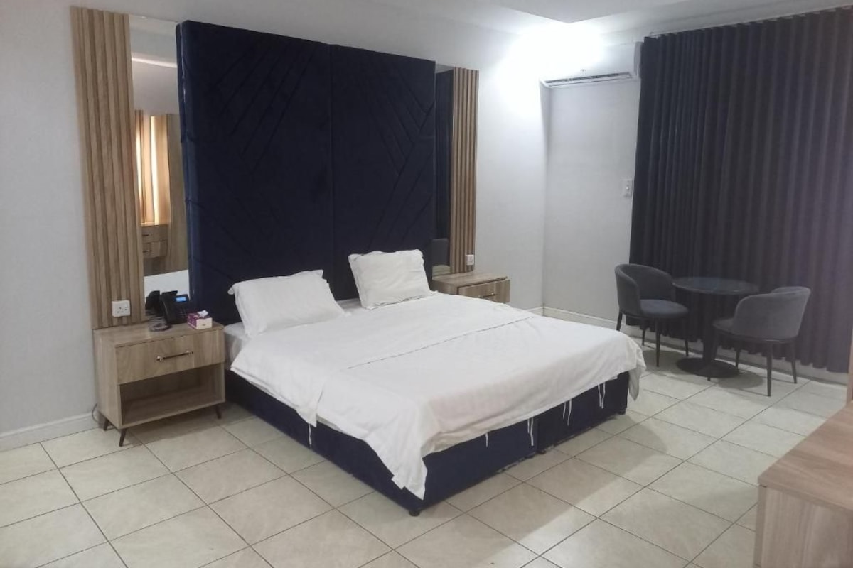 A hotel room with a bed, bedside tables, a desk with chairs, and a wardrobe.