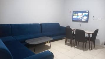 Sala de estar com um sofá azul, uma mesinha de centro e uma mesa de jantar com cadeiras.