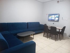 A living area with a blue sofa, a small coffee table, and a dining table with chairs. - Fouad Ali Al-Ezzi for Serviced Apartments Al-Hawiyah (At Taif)