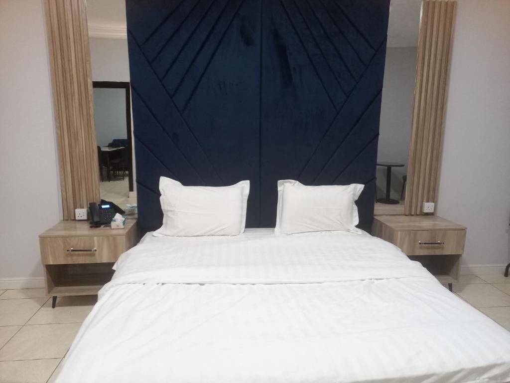 Une chambre d’hôtel avec un lit, deux tables de chevet, un miroir et une tête de lit sombre.