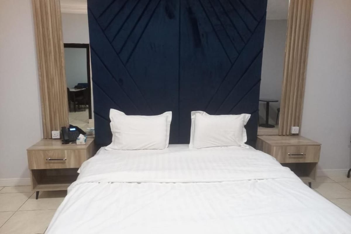 A hotel room with a bed, two bedside tables, a mirror, and a dark headboard.