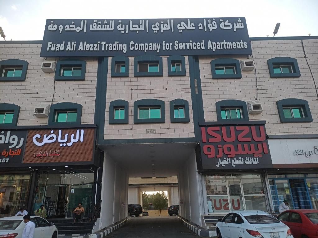 A building with a sign for 'Fuad Ali Alezzi Trading Company for Serviced Apartments' and two storefronts below.