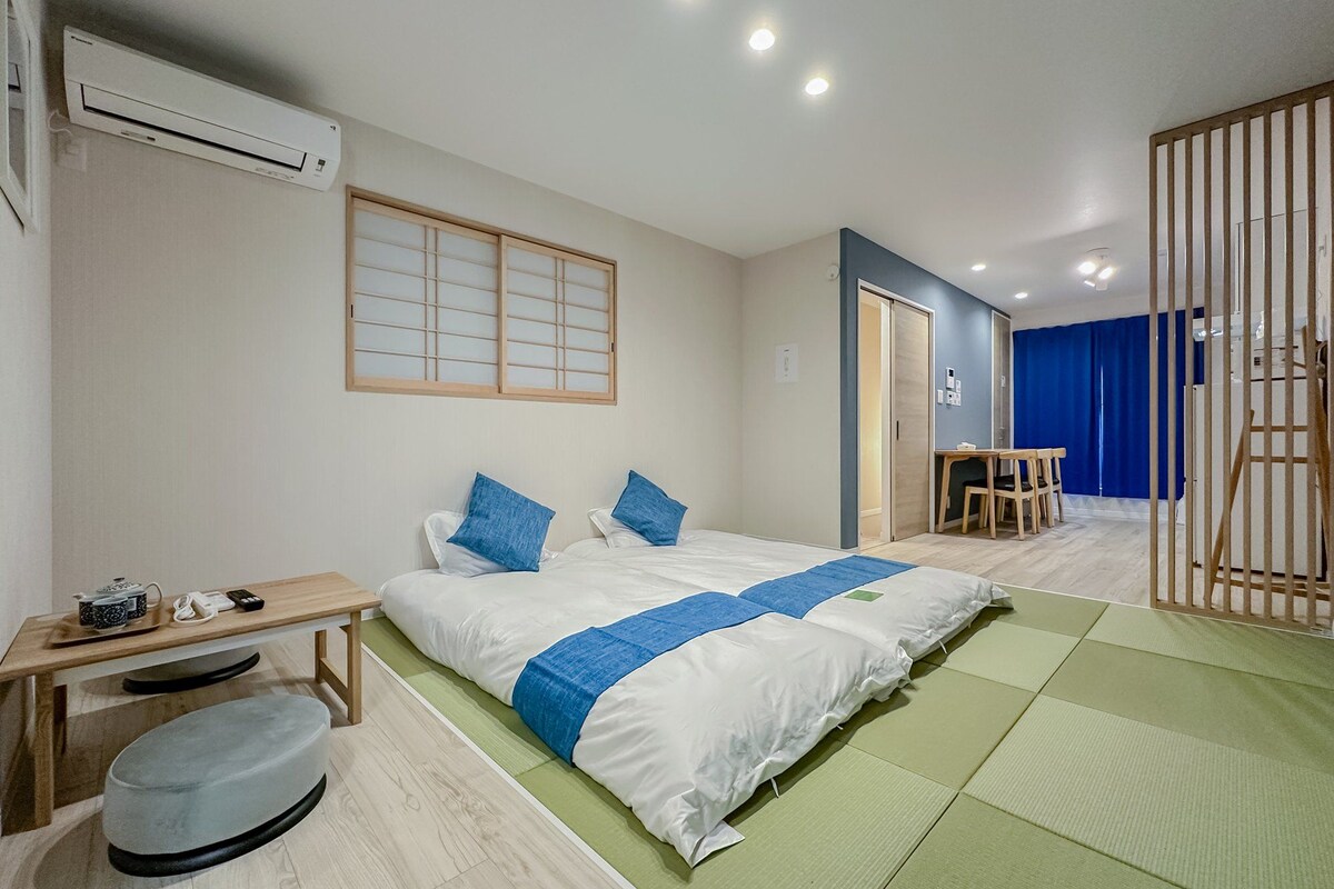 A hotel room with a bed, a desk, a chair, a futon, and a sliding door.