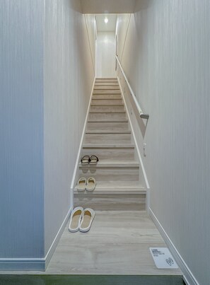 A narrow hallway with a wooden staircase, a handrail, and a pair of shoes placed on the floor. - HANASTAY AYA (Osaka)