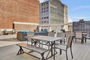 An outdoor patio with tables and chairs, a brick wall, and a modern building in the background. - PremiumStays: Bright, cozy, furnished : Theater : Sports : Parking : Central (Cleveland)
