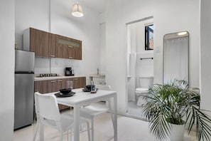 A compact kitchen with white cabinetry, a stainless steel refrigerator, a dining table with two chairs, and a potted plant. - Casa San Rafael Apt 2 | Aesthetic Escape for Two (San Juan de Puerto Rico)