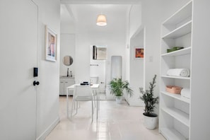 A modern, minimalist hallway with white walls, a dining area with a white table and chairs, and a shelving unit with folded towels. - Casa San Rafael Apt 2 | Aesthetic Escape for Two (San Juan de Puerto Rico)