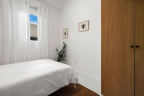 A bedroom with a bed, white curtains, a small window, a plant, and a wooden door. - Casa San Rafael Apt 2 | Aesthetic Escape for Two (San Juan de Puerto Rico)