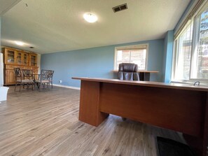 A room with a wooden desk, a chair, a dining area with chairs, a window with blinds, and a ceiling with recessed lighting. - Cheerful 3 bedroom waterfront cottage with WiFi Tv (Selwyn)
