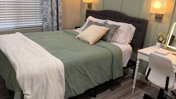 A bedroom with a bed, bedside lamps, a desk with a chair, and a window with blinds and curtains.