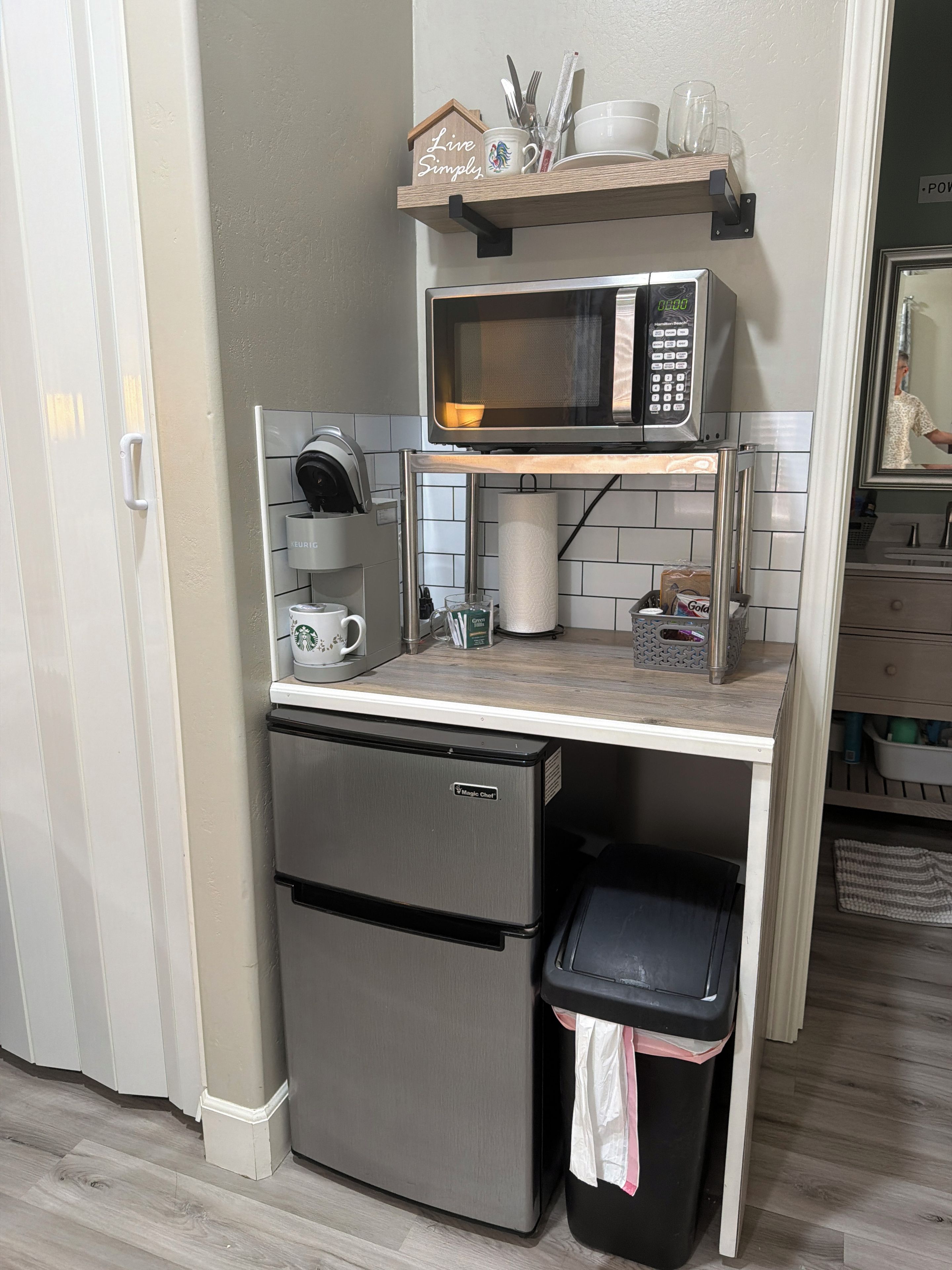 Een compacte kitchenette met een magnetron, koffiezetapparaat en een kleine prullenbak.