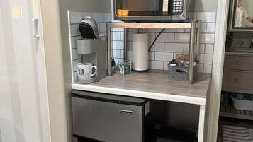 Een compacte kitchenette met een magnetron, koffiezetapparaat en een kleine prullenbak.