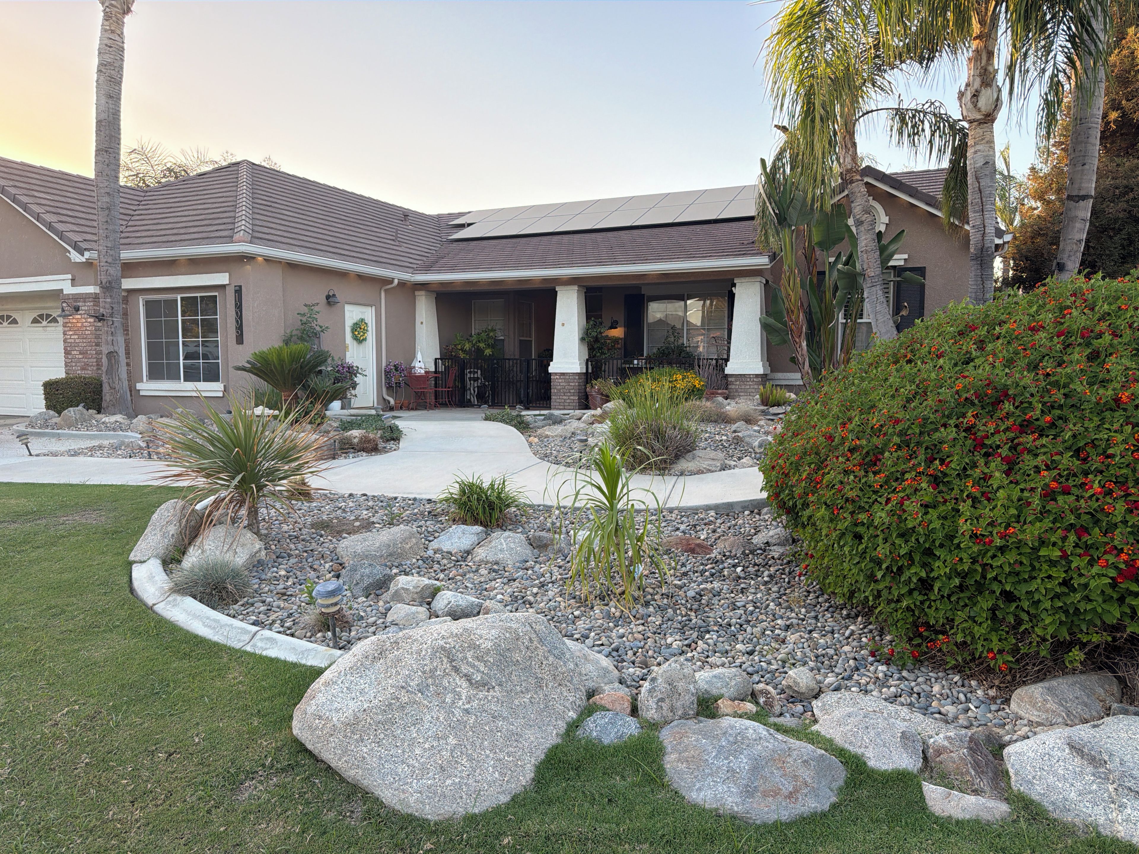 A residential house with a covered patio, a driveway, and a landscaped garden with rocks and plants.
