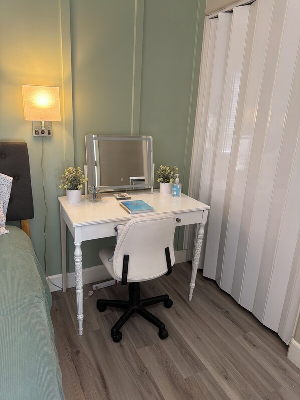 A room with a white desk, a chair, a bed, a lamp, a mirror, and a potted plant.