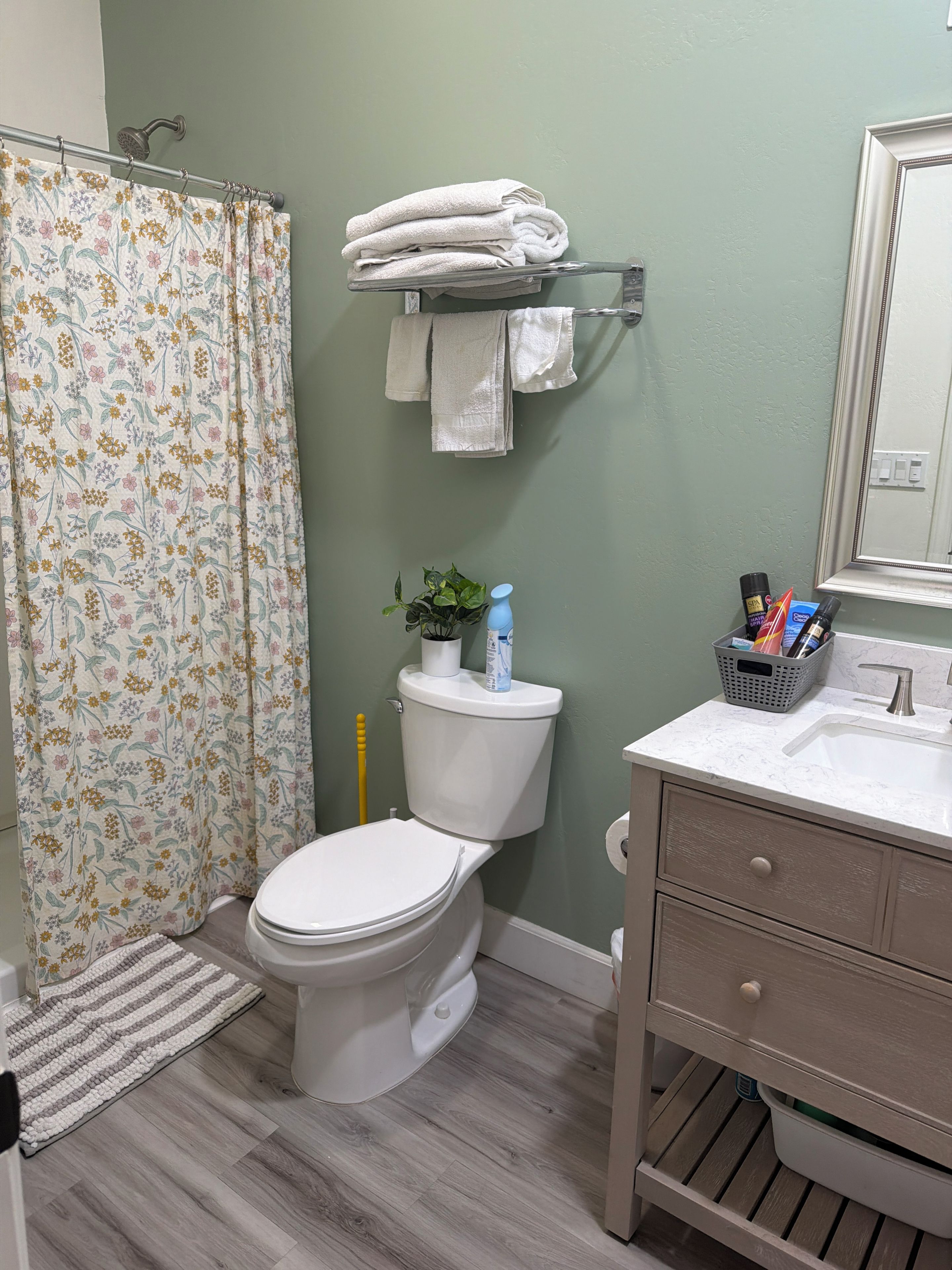 Een badkamer met toilet, wastafel, spiegel, douchegordijn en handdoekrek.