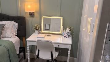 Een slaapkamer met een bed, nachtkastje, lamp en een bureau met stoel.