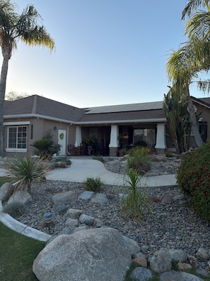 A two-story building with a covered patio area, a stone pathway, and various plants.