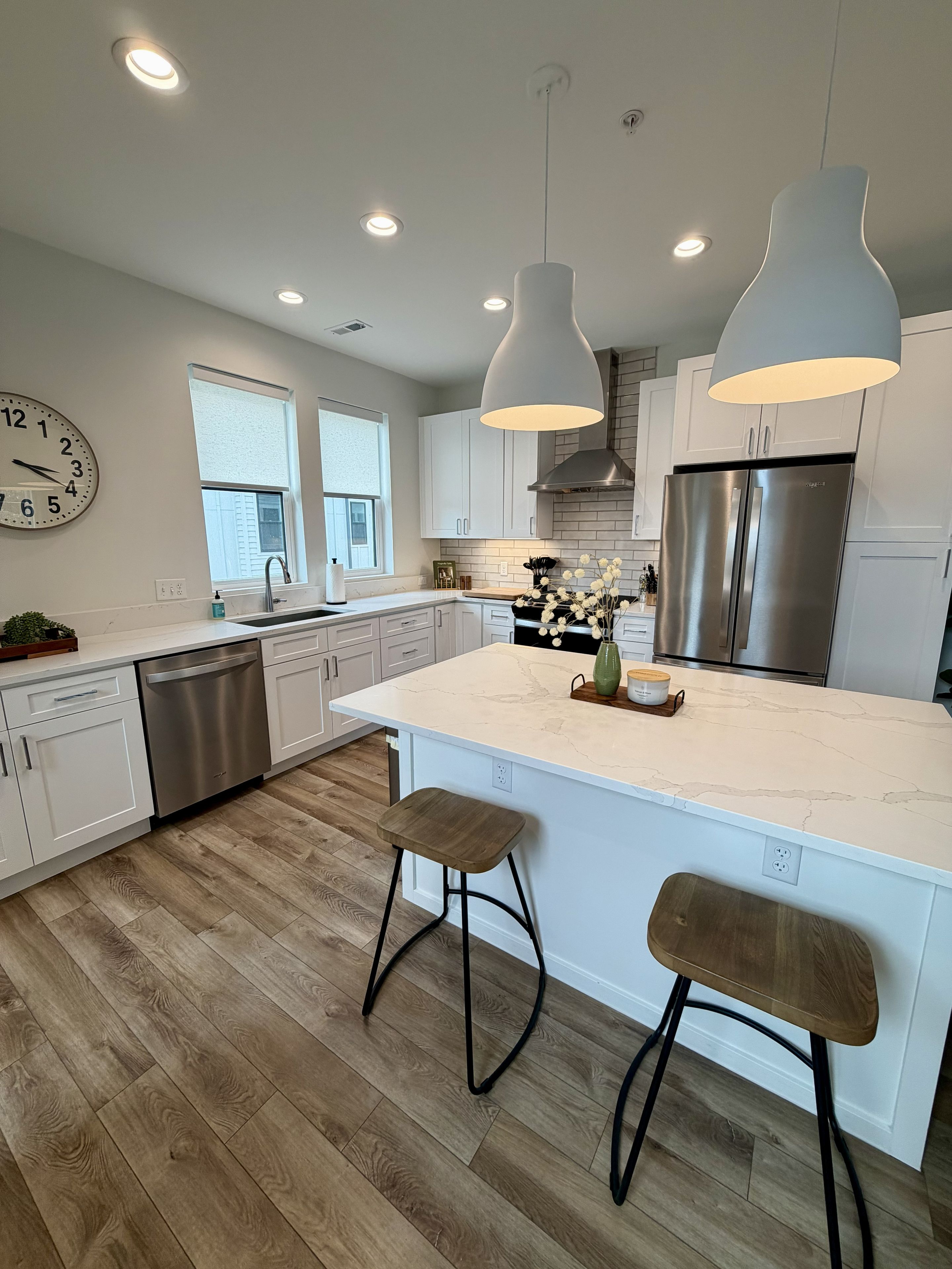 Una cocina moderna con armarios blancos, un refrigerador de acero inoxidable y una isla central con taburetes.
