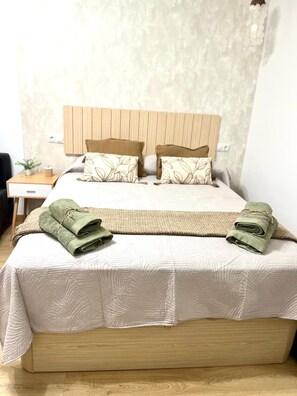 A bed with a wooden headboard, two pillows, a folded green towel, and a bedside table with a plant. - Beautiful Apartment II: Free Welcome Package (Torremolinos)