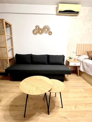 A modern bedroom with a black sofa, a wooden side table, a small bedside table, and a wall-mounted air conditioner. - Beautiful Apartment II: Free Welcome Package (Torremolinos)