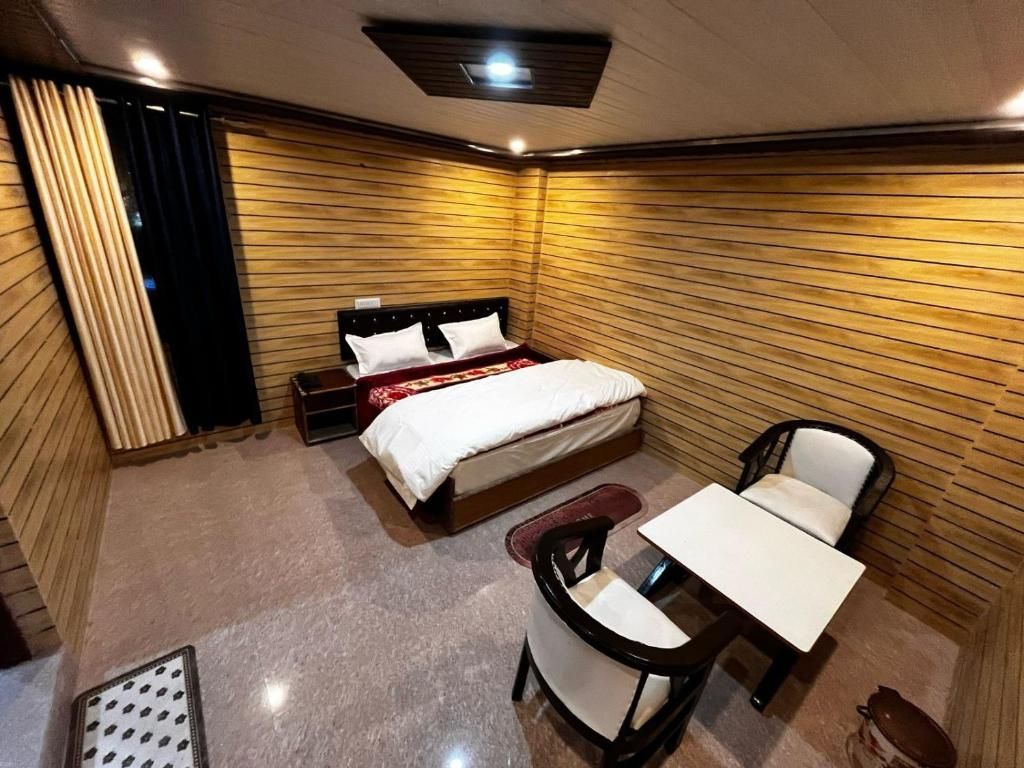 Habitació d'hotel petita amb llit, taula, cadira i finestra amb cortines.