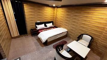 A compact hotel room with a bed, a small table, a chair, and a window with curtains.