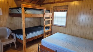 A wooden bunk bed room with a single bed, a chair, and a window with blinds. - Bear Necessities Camping Cabin 3 (West Yellowstone)