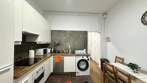 Una cocina compacta con lavadora, un comedor con mesa y sillas, y un reloj en la pared.