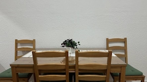 Una mesa de comedor con cuatro sillas de madera, un florero con una planta y un cojín verde en el asiento de una silla.