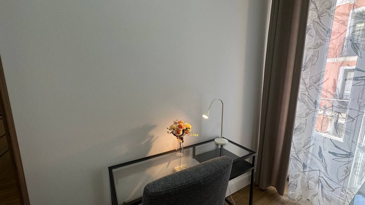 A room with a glass table, a chair, a desk lamp, and a vase with flowers.