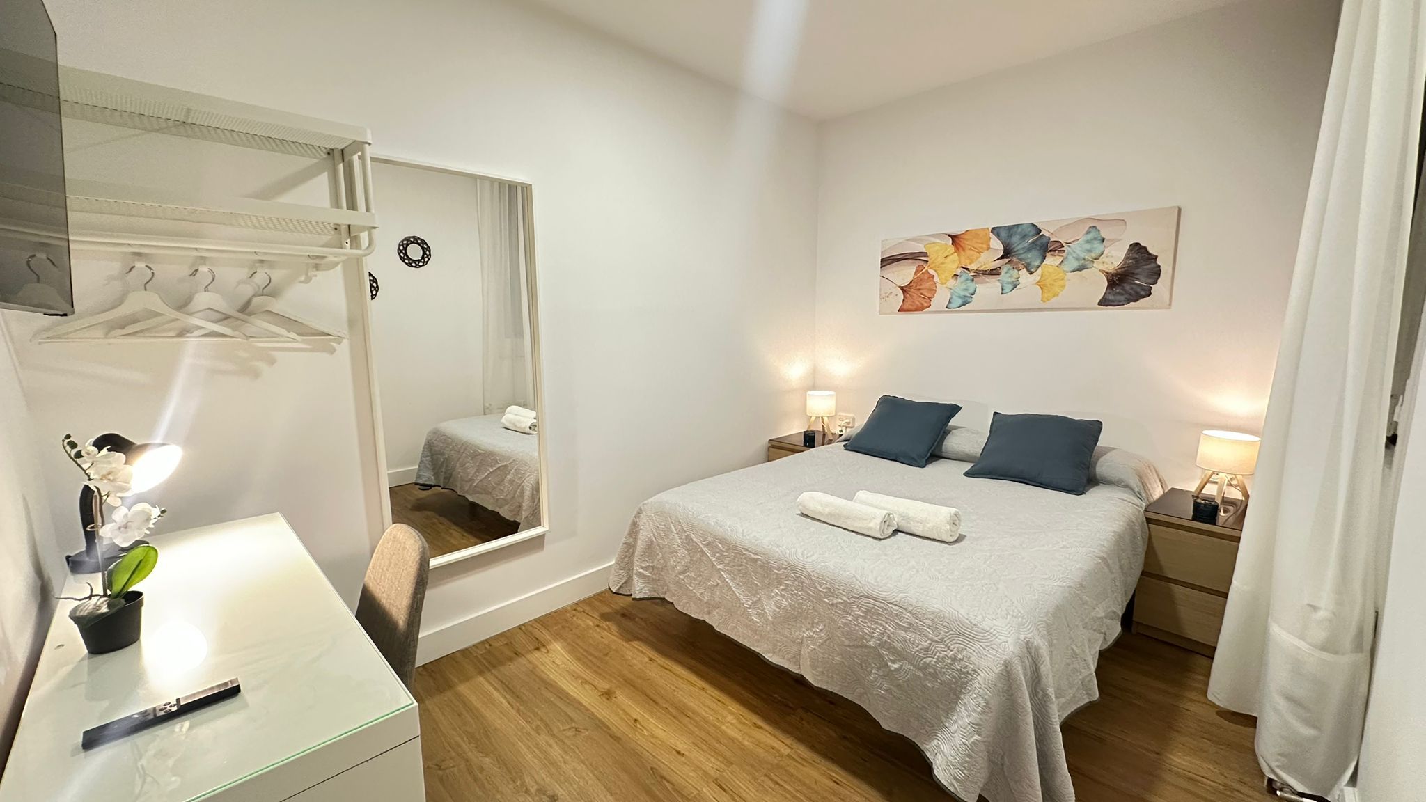 Un dormitorio con cama, mesitas de noche, un espejo y un cuadro en la pared.