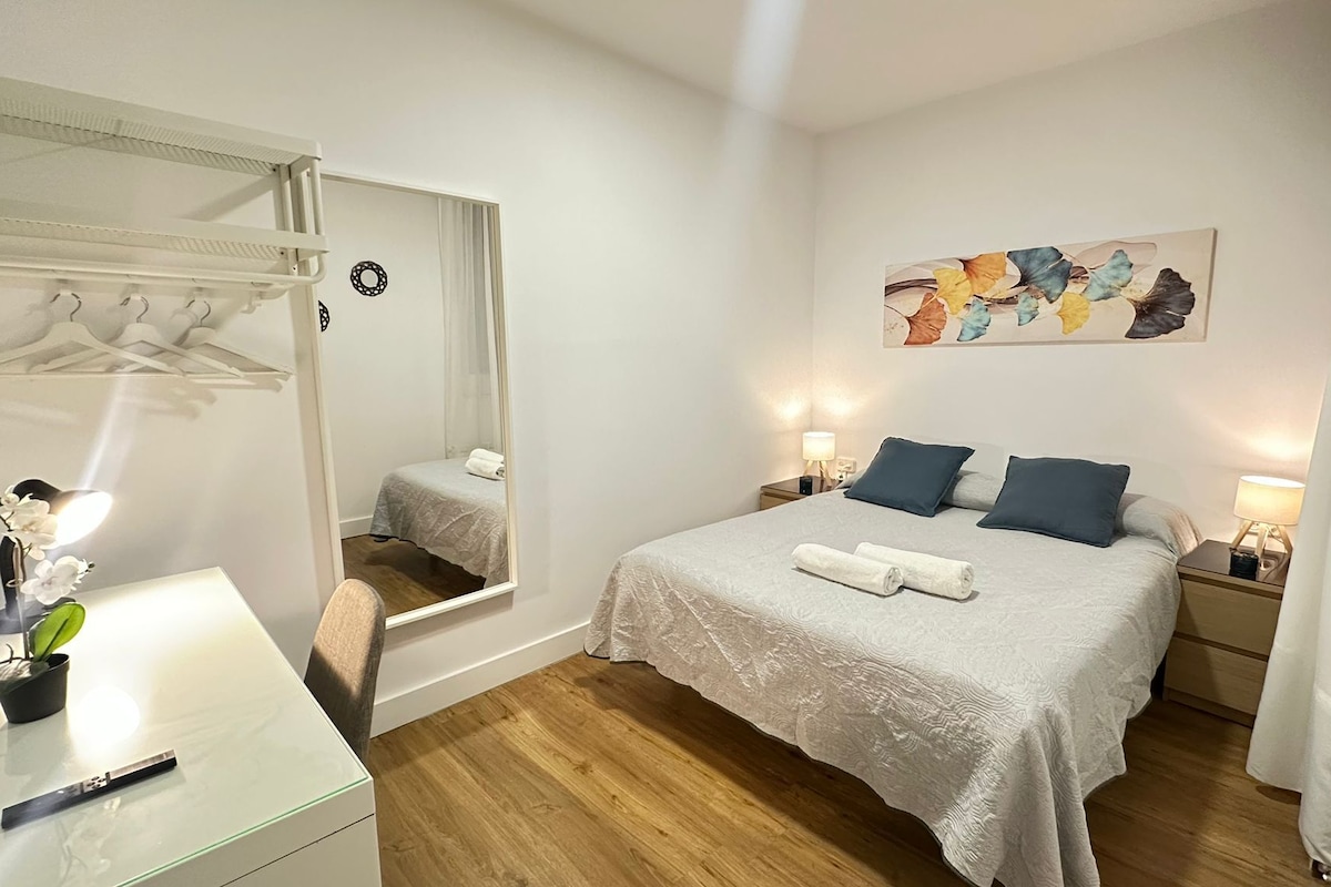 Un dormitorio con cama, mesitas de noche, un espejo y un cuadro en la pared.