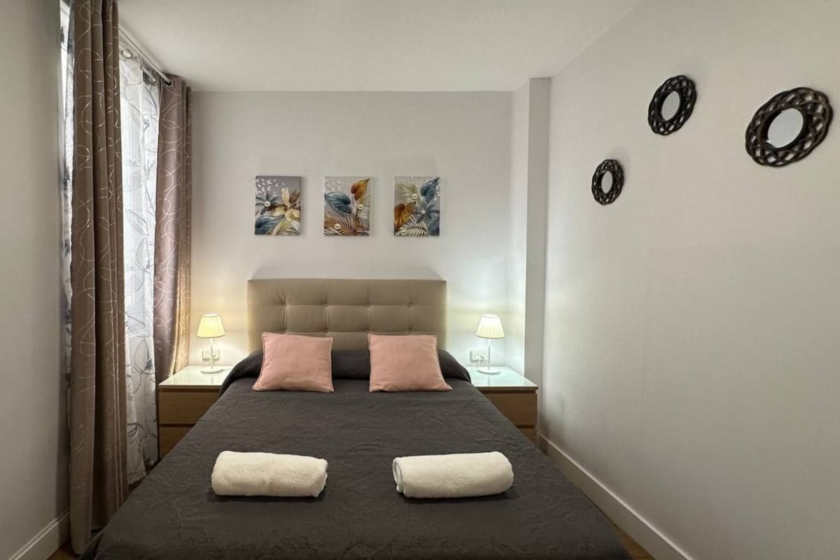 A bedroom with a large bed, two bedside tables with lamps, a headboard, and three wall-mounted artworks.