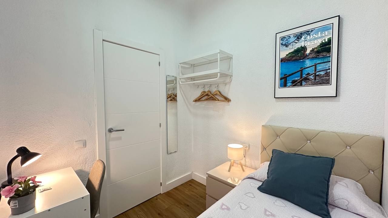 Een slaapkamer met een bed, nachtkastje, lamp, stoel, kledingkast en een lijst aan de muur.